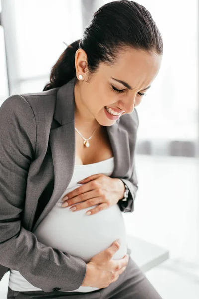 Donna incinta che sopporta il dolore e siede sul tavolo in ufficio — Foto stock