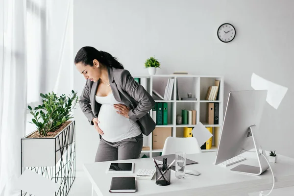 Exhausted pregnant woman standing in office and enduring pain — Stock Photo