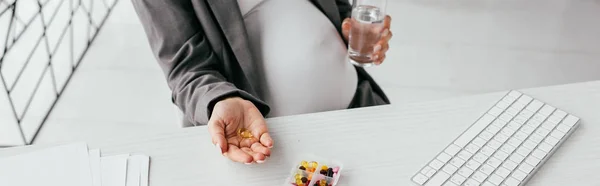 Panoramic shot of pregnant woman holding pools while sitting behind table — Stock Photo