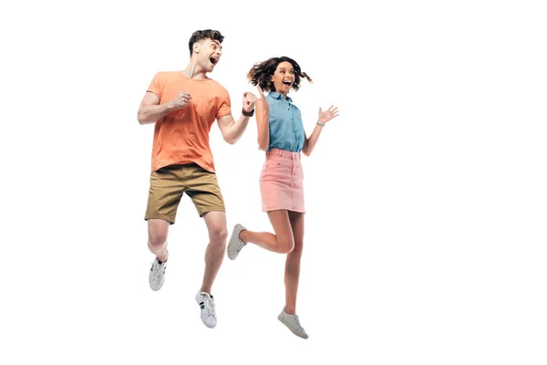 Feliz hombre y mujer saltando y mirando hacia otro lado mientras muestra sí gesto aislado en blanco - foto de stock