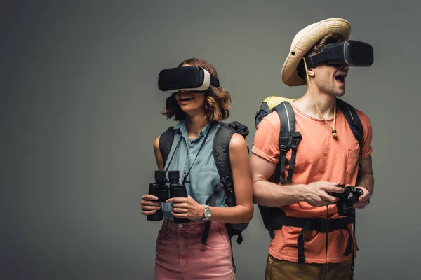 Two excited tourists with binoculars and digital camera using virtual reality headsets on grey background — Stock Photo