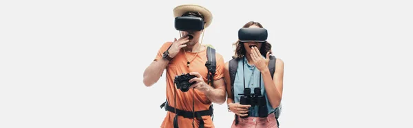 Panoramic shot of two surprised tourists using virtual reality headsets isolated on grey — Stock Photo