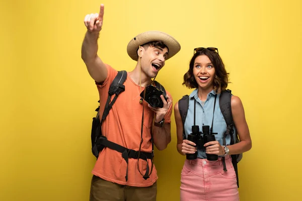 Cheerful man pointing with finger while standing near smiling young woman on yellow background — Stock Photo