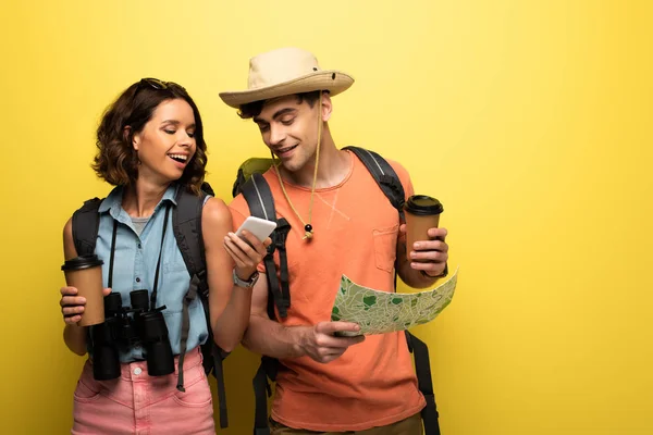 Веселая женщина показывает смартфон мужчине с географической картой на желтом фоне — стоковое фото