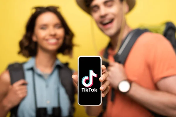 KYIV, UKRAINE - JUNE 3, 2019: Selective focus of cheerful woman showing smartphone with Tik Tok app while standing near smiling man on yellow background. — Stock Photo
