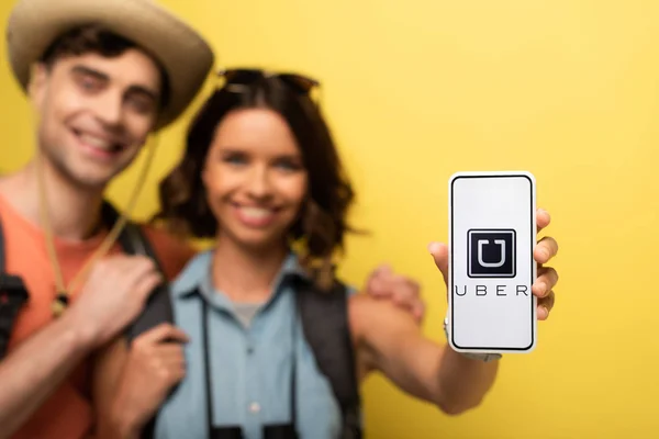 KYIV, UCRAINA - GIUGNO 3, 2019: Focus selettivo della ragazza sorridente che mostra lo smartphone con l'app Uber mentre si trova vicino al fidanzato allegro su sfondo giallo . — Foto stock