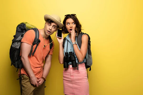 Chocado jovem segurando smartphone com tela em branco perto de homem pensativo no fundo amarelo — Fotografia de Stock