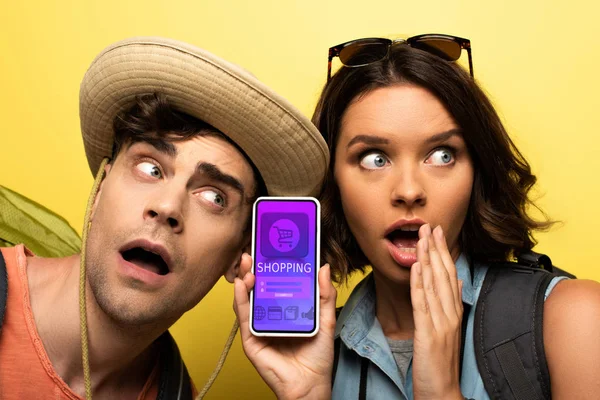 Shocked young woman showing smartphone with shopping app while standing near suprised man on yellow background — Stock Photo