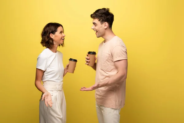 Smiling man and woman talking while holding paper cups on yellow background — Stock Photo