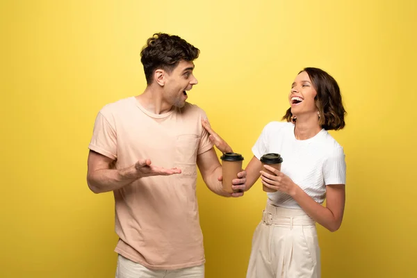 Excité homme et femme parler tout en tenant du café pour aller sur fond jaune — Photo de stock
