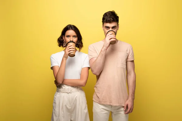 Junger Mann und Frau trinken Kaffee to go, während Kaffee zu gehen auf gelbem Hintergrund — Stockfoto