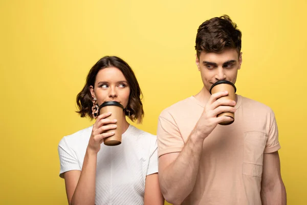 Homem positivo e mulher olhando um para o outro enquanto bebe café para ir no fundo amarelo — Fotografia de Stock