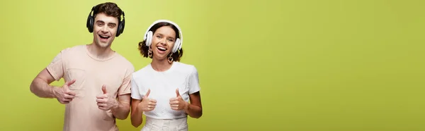 Plano panorámico de hombre y mujer emocionados sonriendo a la cámara y mostrando los pulgares hacia arriba sobre fondo verde - foto de stock