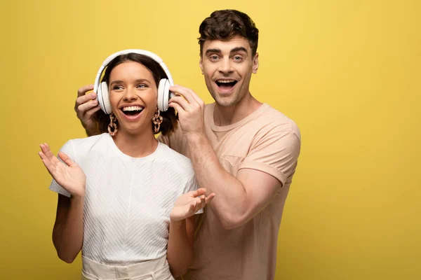 Homme souriant mettre des écouteurs sur fille gaie sur fond jaune — Photo de stock