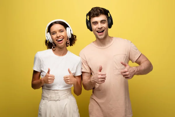 Homem alegre e mulher mostrando polegares para cima enquanto sorrindo para a câmera no fundo amarelo — Fotografia de Stock