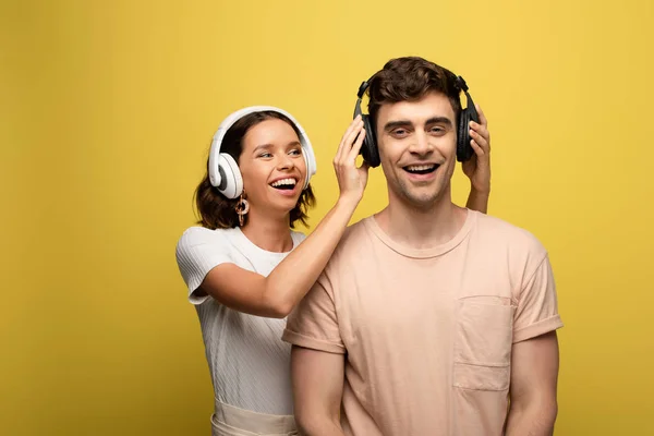 Feliz joven mujer que se pone los auriculares en el hombre alegre sobre fondo amarillo - foto de stock