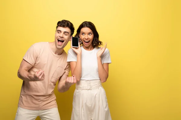 Happy young man showing yes gesture while standing near excited girl on yellow background — Stock Photo