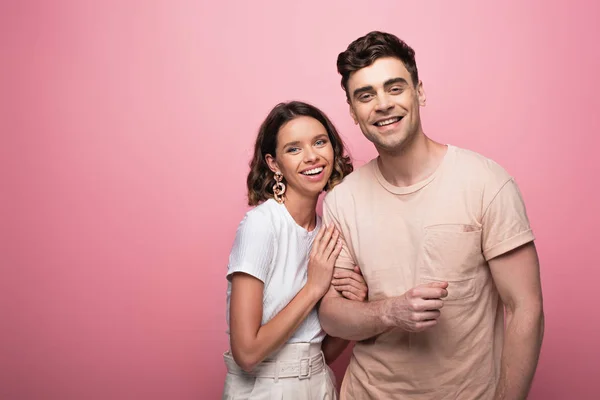 Feliz joven mujer abrazando feliz novio en rosa fondo — Stock Photo