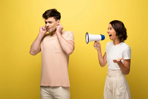 Irritated girl quarreling in loudspeaker at boyfriend on yellow background — Stock Photo