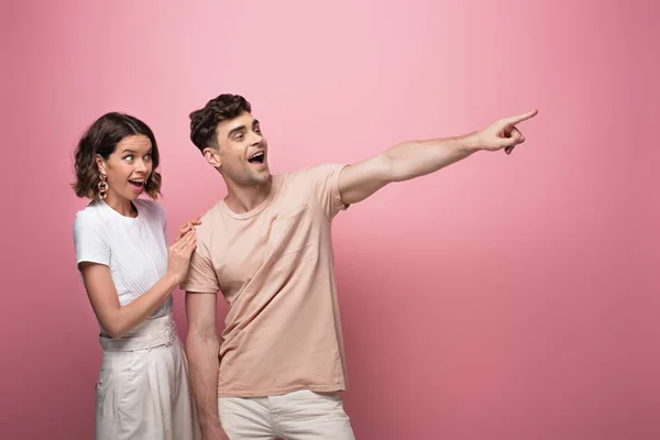 Excited man pointing with finger near surprised woman on pink background — Stock Photo
