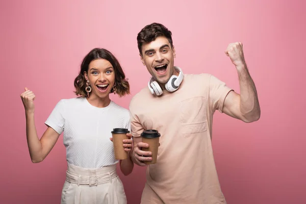 Aufgeregter Mann und Frau mit Ja-Gesten, während sie Pappbecher in die Kamera auf rosa Hintergrund halten — Stockfoto