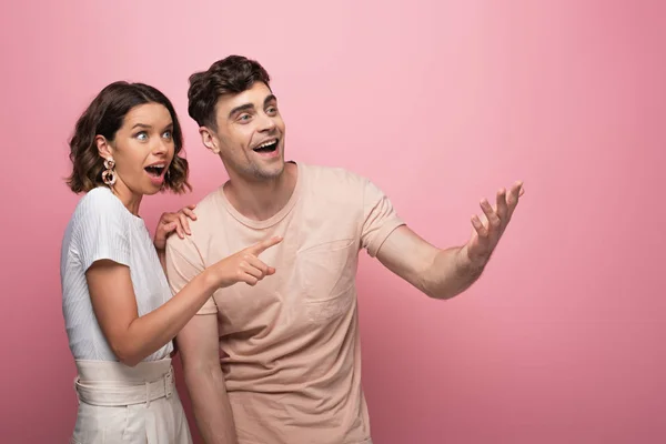 Молодой, взволнованный мужчина и женщина улыбаются и смотрят в сторону на розовый фон — стоковое фото