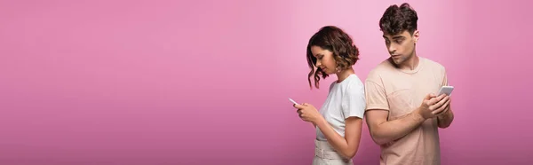 Panoramic shot of young man and woman using smartphones on purple background — Stock Photo