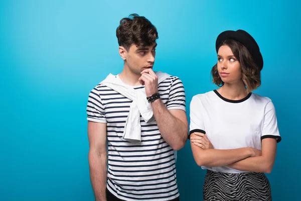 Joven, hombre y mujer de moda mirándose el uno al otro sobre fondo azul - foto de stock