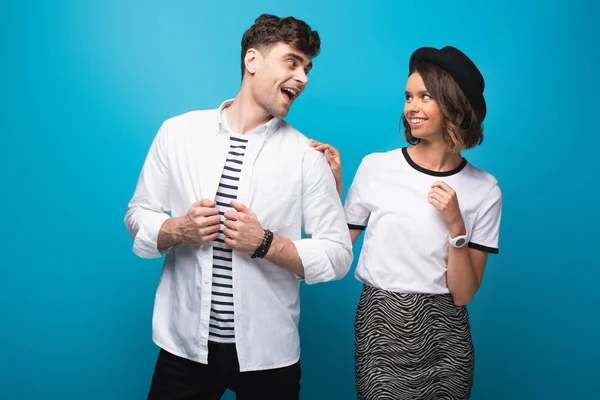 Joyeux, homme et femme à la mode qui se regardent sur fond bleu — Photo de stock