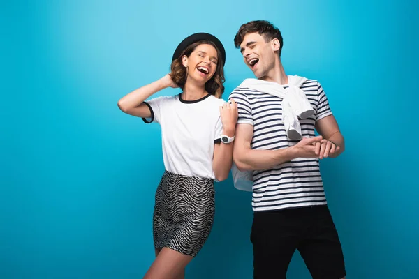 Junges, fröhliches Paar lacht gemeinsam auf blauem Hintergrund — Stockfoto
