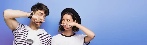 Tiro panorâmico de homem positivo e mulher segurando dedos com bigode desenhado perto de rostos no fundo azul — Fotografia de Stock