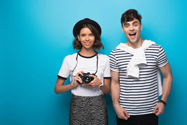 Smiling girl with digital camera and cheerful man looking at camera on blue background — Stock Photo