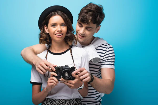 Hombre atento ajustando la cámara digital de la novia sonriente sobre fondo azul - foto de stock