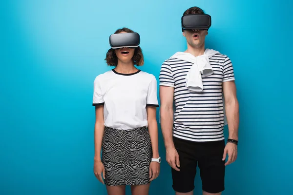 Joven, hombre y mujer de moda utilizando auriculares de realidad virtual sobre fondo azul - foto de stock