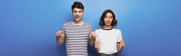 Plano panorámico del hombre y la mujer mirando hacia abajo y señalando con los dedos sobre fondo azul — Stock Photo