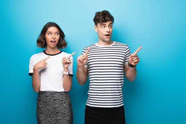 Cheerful man and woman looking away and pointing with fingers on blue background — Stock Photo