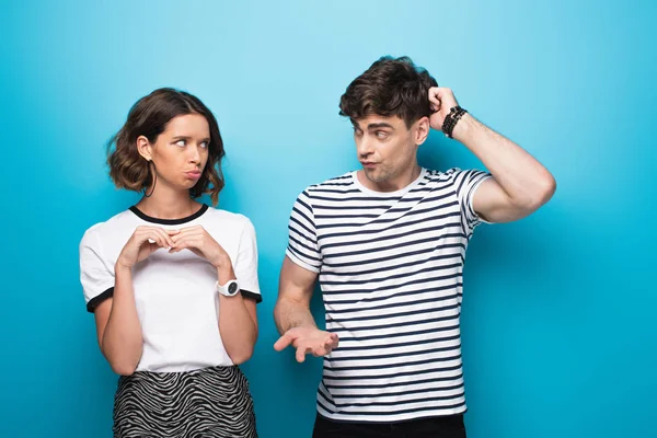 Discouraged man looking at offended girlfriend on blue background — Stock Photo