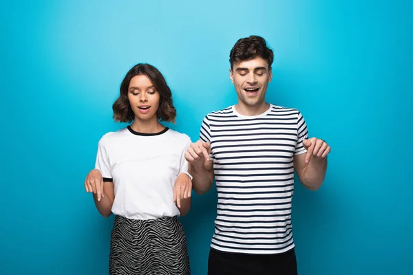 Young man and woman looking down and pointing with fingers on blue background — Stock Photo