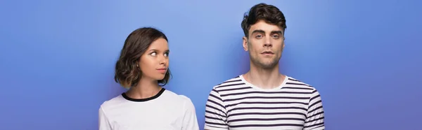 Panoramic shot of positive young girl looking at offended boyfriend on blue background — Stock Photo