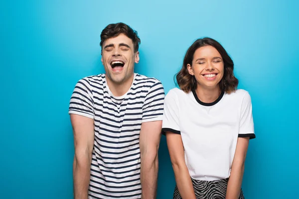 Excité homme et femme riant avec les yeux fermés sur fond bleu — Photo de stock