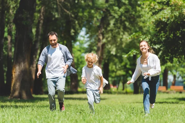 Glückliche Familie läuft tagsüber im Park und schaut in die Kamera — Stockfoto