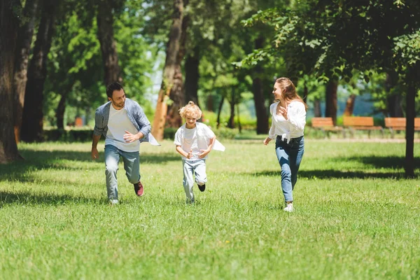 Familia feliz en ropa casual corriendo en el parque durante el día - foto de stock