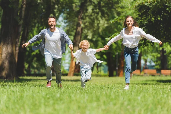 Familia sonriente cogida de la mano y corriendo en el parque durante el día - foto de stock