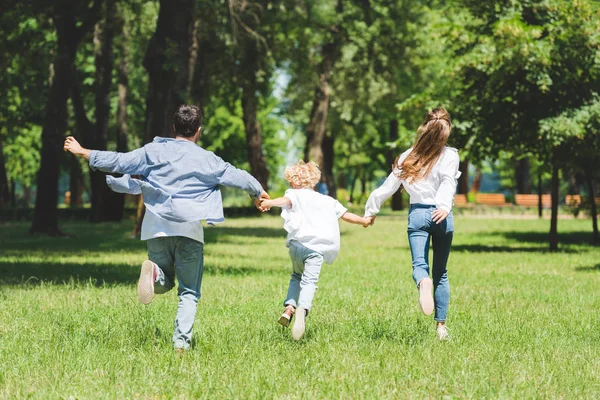 Happy family holding hands and running in park during daytime — Stock Photo