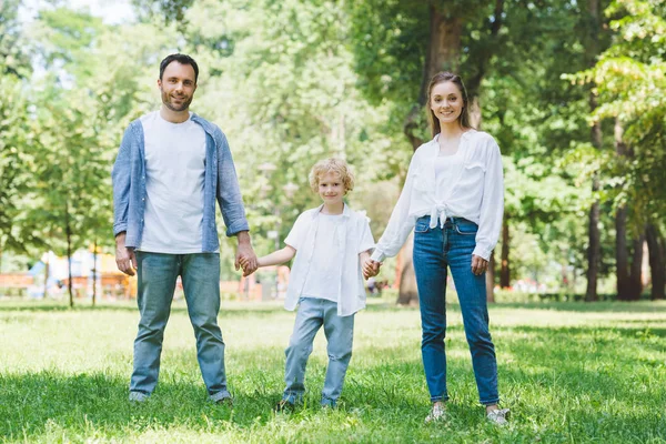Щаслива сім'я дивиться на камеру і тримає руки в парку — стокове фото