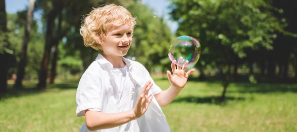 Tiro panorâmico de menino bonito Gesturing perto de bolhas de sabão no parque — Fotografia de Stock
