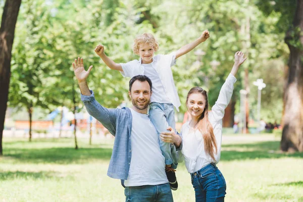 Familia feliz con las manos extendidas mirando a la cámara en el parque - foto de stock