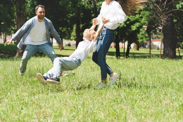 Family spending time together, woman spinning son in park — Stock Photo