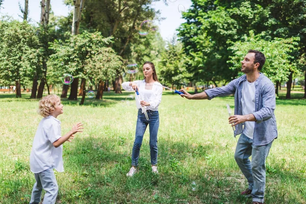 Mãe, pai e filho brincando com bolhas de sabão no parque durante o dia — Fotografia de Stock