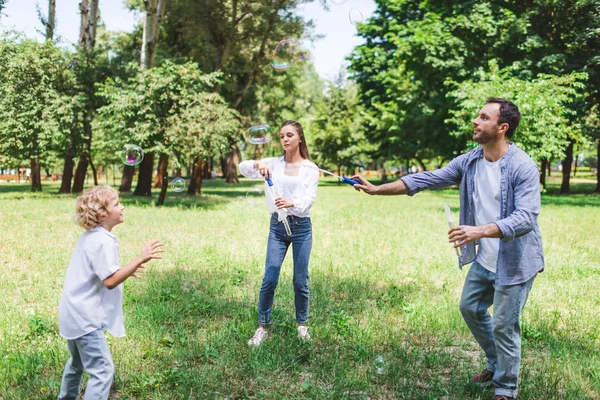 Mère, père et fils jouant avec des bulles de savon dans le parc pendant la journée — Photo de stock